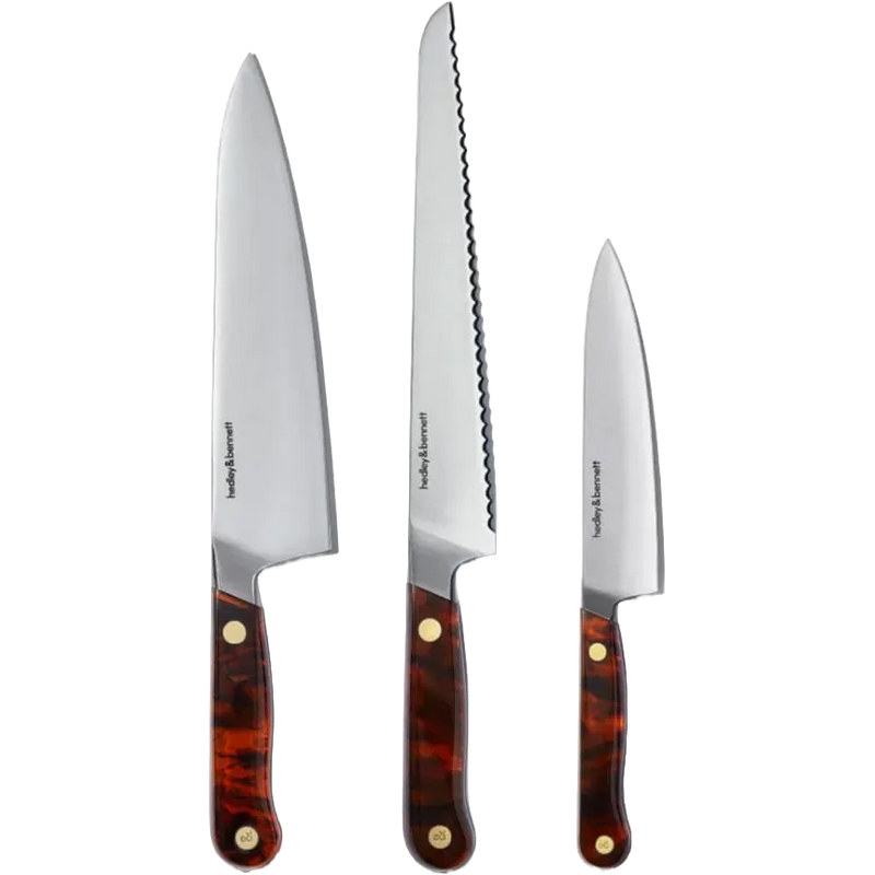 Three Hedley & Bennett kitchen knives with silver stainless steel blades and tortoiseshell-patterned brown handles with brass rivets, displayed vertically against a white background.