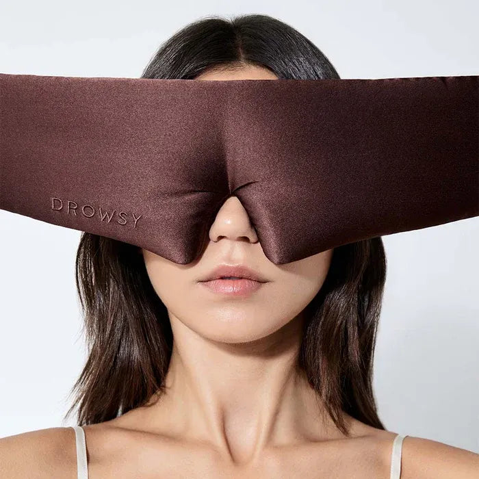 Person wearing a brown sleep mask with 'Drowsy' branding on a white background