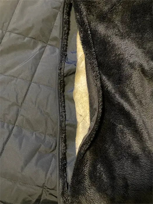 Close-up of the Eddie Bauer Quilted Insulated Fleece Blanket with the embroidery access pocket open, showing the quilted shell and fleece lining for custom embroidery