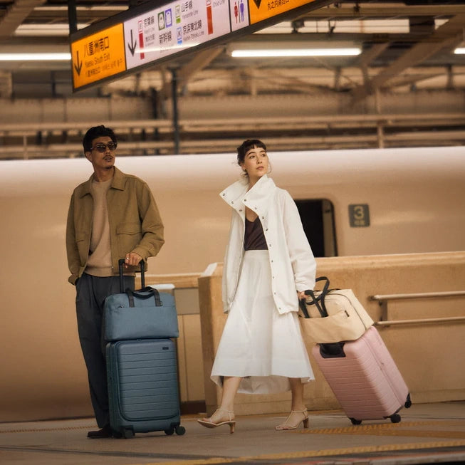 Two people with luggage standing in a train station.