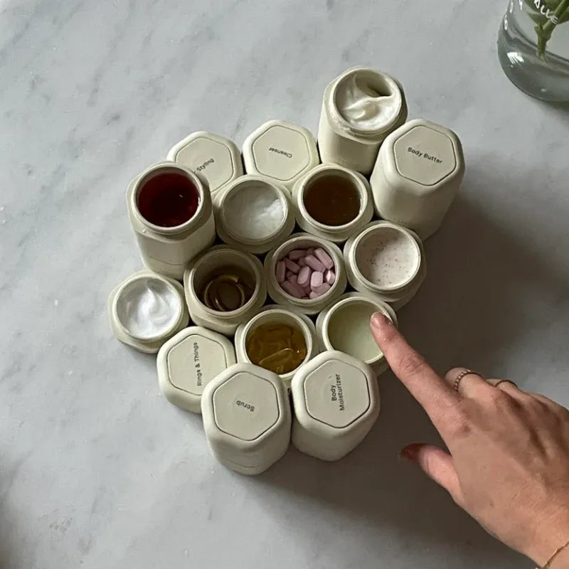 Set of small containers with labels on a marble surface, with a hand pointing to one of them.