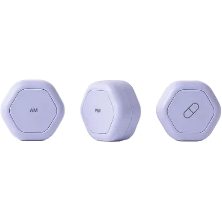 Three small round pill tracker devices in a pale lavender color, shown from different angles on a plain white background. The left device is labeled 'AM', the center device is labeled 'PM', and the right device has a capsule icon.