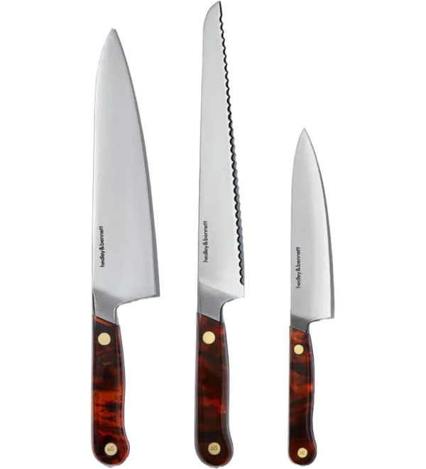 Three Hedley & Bennett kitchen knives with silver stainless steel blades and tortoiseshell-patterned brown handles with brass rivets, displayed vertically against a white background.