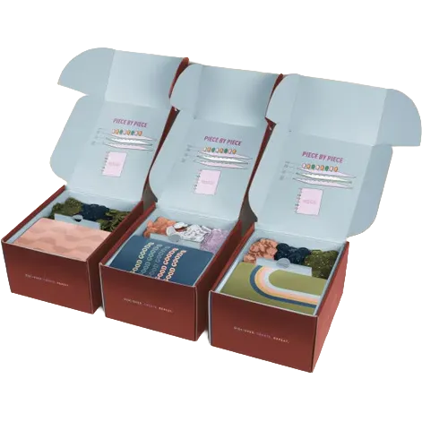 Three open gift boxes arranged side by side on a white background, each containing folded knit socks in different colors and patterns. The boxes are dark red-brown with pale blue inner flaps, and the socks include pastel pink, blue, green, and multicolor designs.