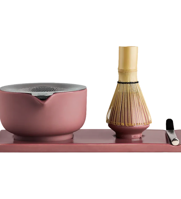 Fellow matcha tea set on a rectangular tray, featuring a dusty pink ceramic bowl with a metal lid, a bamboo whisk, and a small metal scoop on a solid white background.