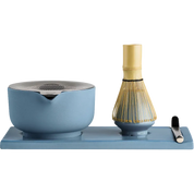 Fellow matcha tea set on a rectangular blue tray, featuring a light blue ceramic whisk bowl with a metal strainer lid, a bamboo whisk with gold-colored tines, and a small black-handled tool, all photographed on a white background.