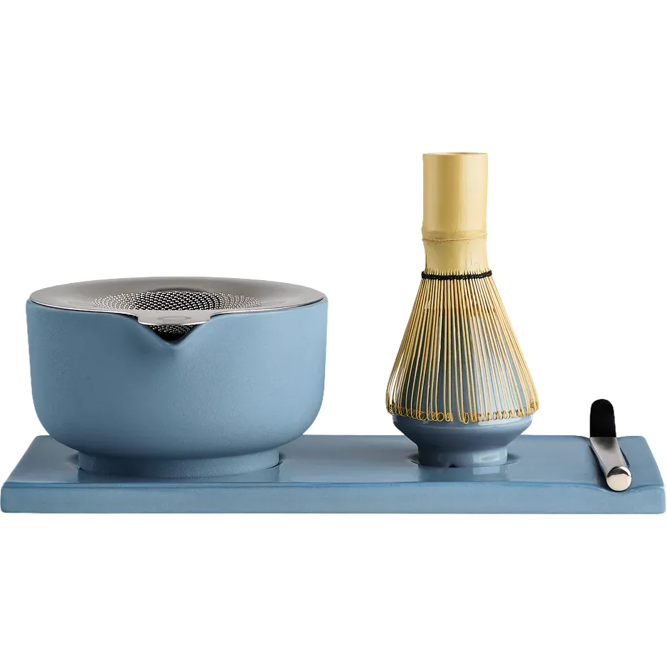 Fellow matcha tea set on a rectangular blue tray, featuring a light blue ceramic whisk bowl with a metal strainer lid, a bamboo whisk with gold-colored tines, and a small black-handled tool, all photographed on a white background.