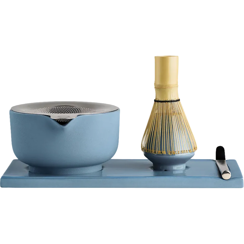 Fellow matcha tea set on a rectangular blue tray, featuring a light blue ceramic whisk bowl with a metal strainer lid, a bamboo whisk with gold-colored tines, and a small black-handled tool, all photographed on a white background.