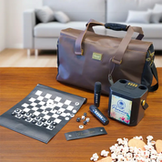 A brown leather-look duffel bag sits on a wooden table with a game set and party accessories arranged in front, including a checkers board, microphone, speaker, popcorn, and a small card. A blurred living room with a sofa is visible in the background.