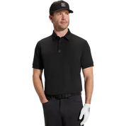 A man modeling a black short-sleeve polo shirt with a small square logo patch on the chest, paired with a black cap, dark pants, and a white golf glove, against a solid white background.