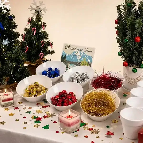 A festive Christmas-themed table setup with bowls of colorful ornaments, tinsel, candles, and miniature decorated trees on a white tablecloth with star confetti.