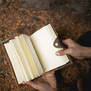 Hand holding an open leather-bound book against a natural background