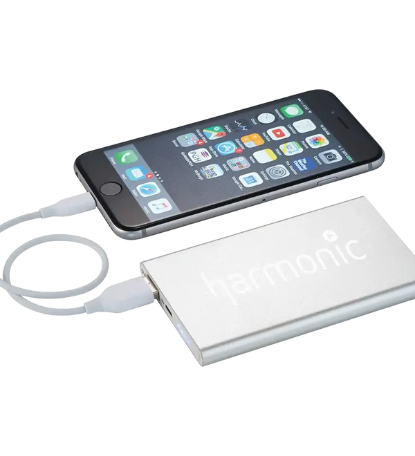 A silver Harmonic portable power bank shown with a smartphone connected via a white cable, on a clean white background.