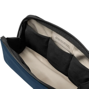 Close-up of the open interior of a blue and black bag, showing a black zipper, black fabric divider, and a cream-colored interior label.