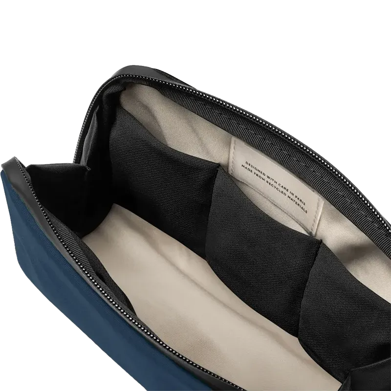 Close-up of the open interior of a blue and black bag, showing a black zipper, black fabric divider, and a cream-colored interior label.