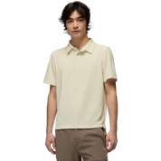 A man wearing a light cream-colored short-sleeve polo shirt and brown pants, standing against a solid white background.