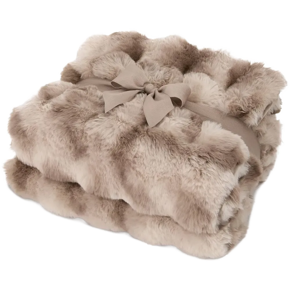 A folded faux fur throw blanket in a warm taupe-beige color, tied with a matching fabric ribbon and bow, on a solid white background.