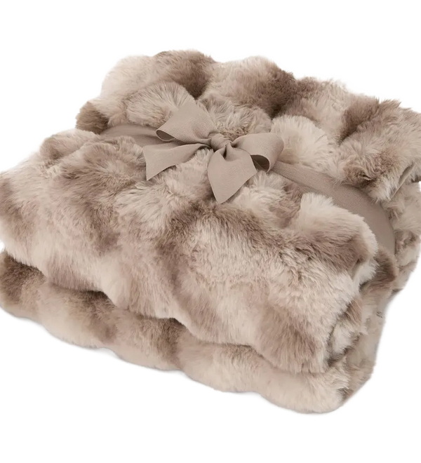 A folded faux fur throw blanket in a warm taupe-beige color, tied with a matching fabric ribbon and bow, on a solid white background.