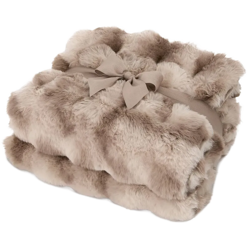 A folded faux fur throw blanket in a warm taupe-beige color, tied with a matching fabric ribbon and bow, on a solid white background.