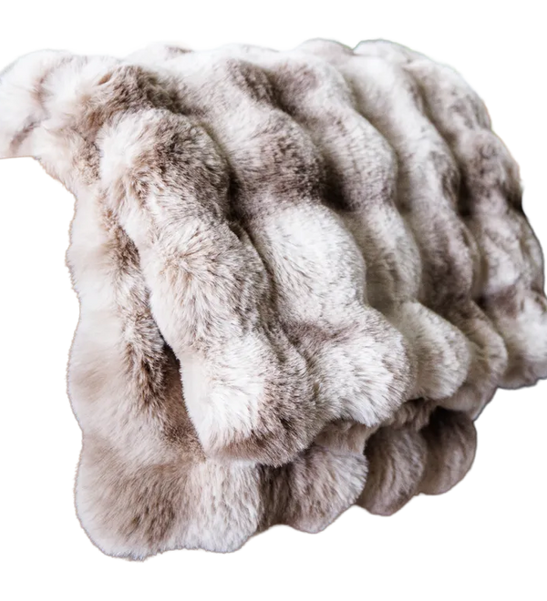 A plush faux fur throw blanket with a wavy, ribbed texture in shades of beige, cream, and light brown, isolated on a white background.