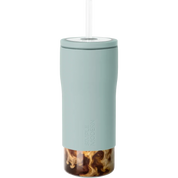 A tall, slim travel tumbler in a muted sage green color with a clear lid and straw, shown on a solid white background. The bottom portion of the tumbler is transparent, revealing a swirl of iced coffee inside.