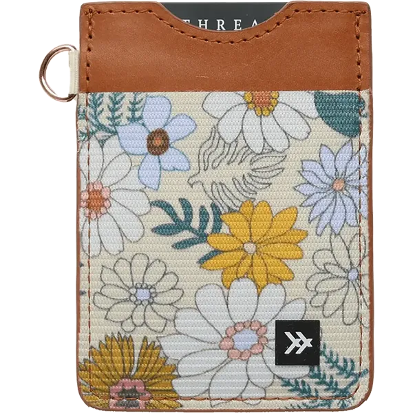 A Thread card holder wallet featuring a tan leather top section and a cream-colored woven fabric body with a colorful floral pattern. It has a small metal ring on the left side and a black brand patch on the bottom right.

